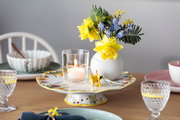 Ein elegant gedeckter Tisch mit einem Wasserglas Boston im Vordergrund, umgeben von Geschirr und einer Blumenvase. Perspektive: seitlich.