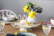 Ein elegant gedeckter Tisch mit einem Wasserglas Boston im Vordergrund, umgeben von Geschirr und einer Blumenvase. Perspektive: seitlich.