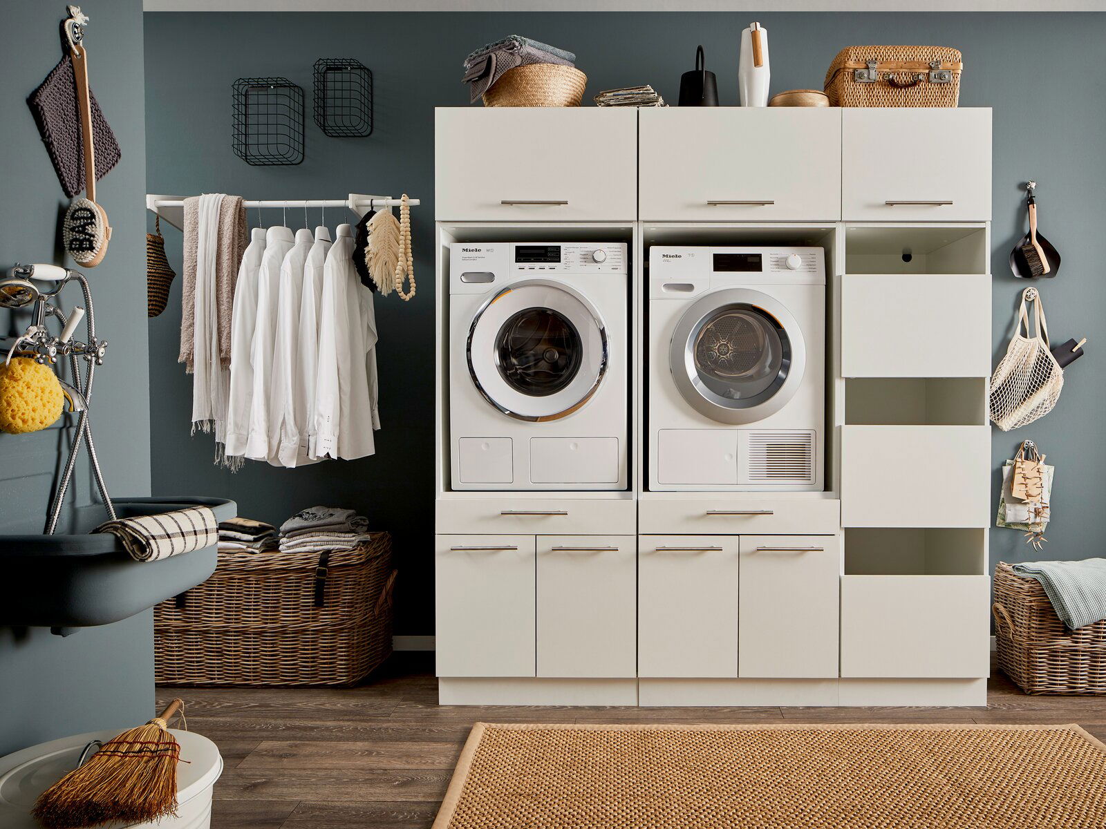 Hauswirtschaftsraum mit Waschmaschine und Trockner in einem modernen Schrank, umgeben von Körben und Wäscheleinen, aus der Frontalperspektive.