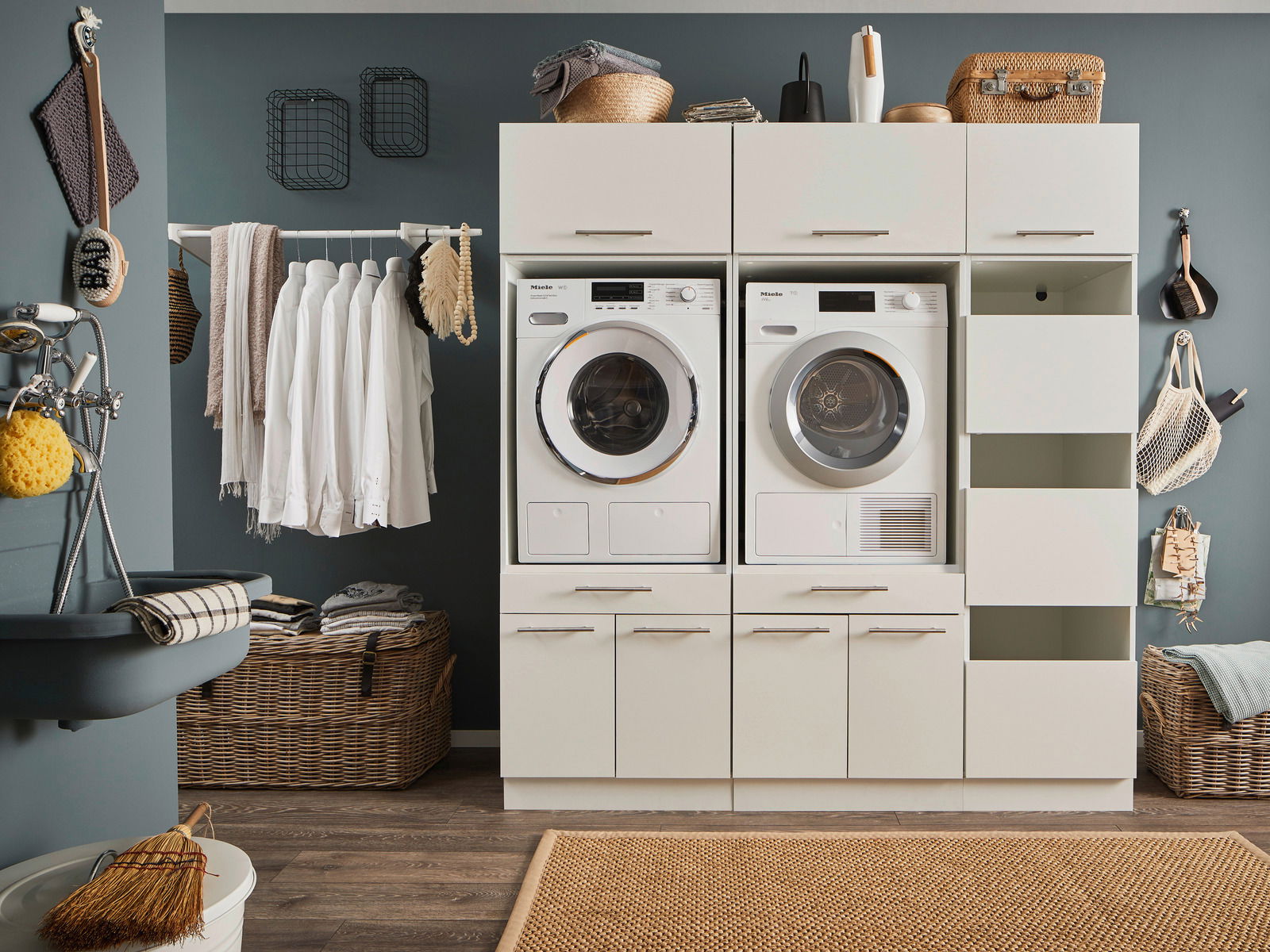Hauswirtschaftsraum mit Waschmaschine und Trockner in einem modernen Schrank, umgeben von Körben und Wäscheleinen, aus der Frontalperspektive.