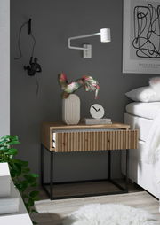 Moderne Nachtkommode aus Holz mit geriffelter Front und schwarzem Metallgestell, dekoriert mit einer Vase und einer Uhr, seitliche Perspektive.