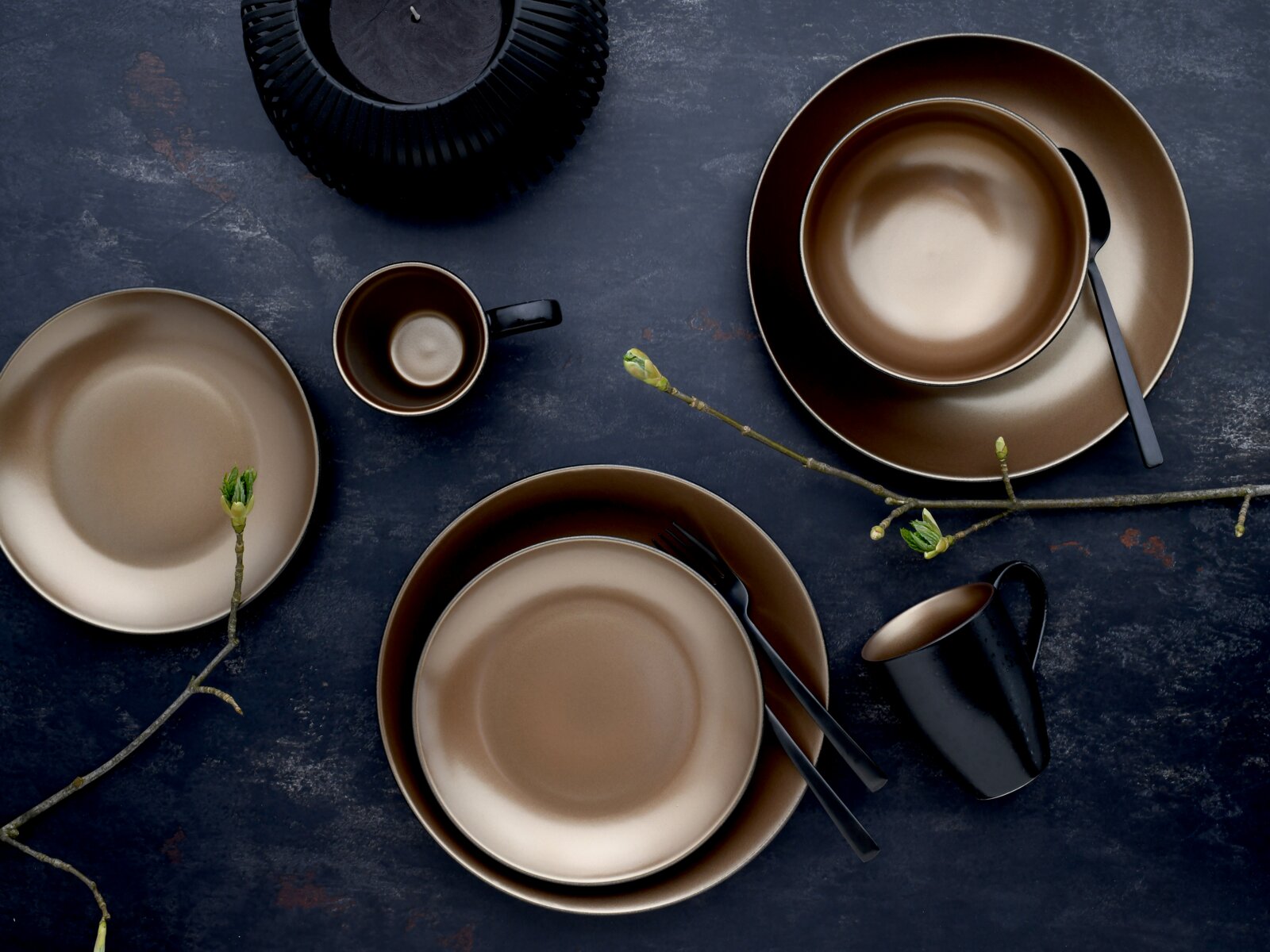 Modernes Geschirr-Set in Braun- und Schwarztönen mit Tellern, Schalen und Tassen auf dunklem Untergrund, Draufsicht (Flatlay)