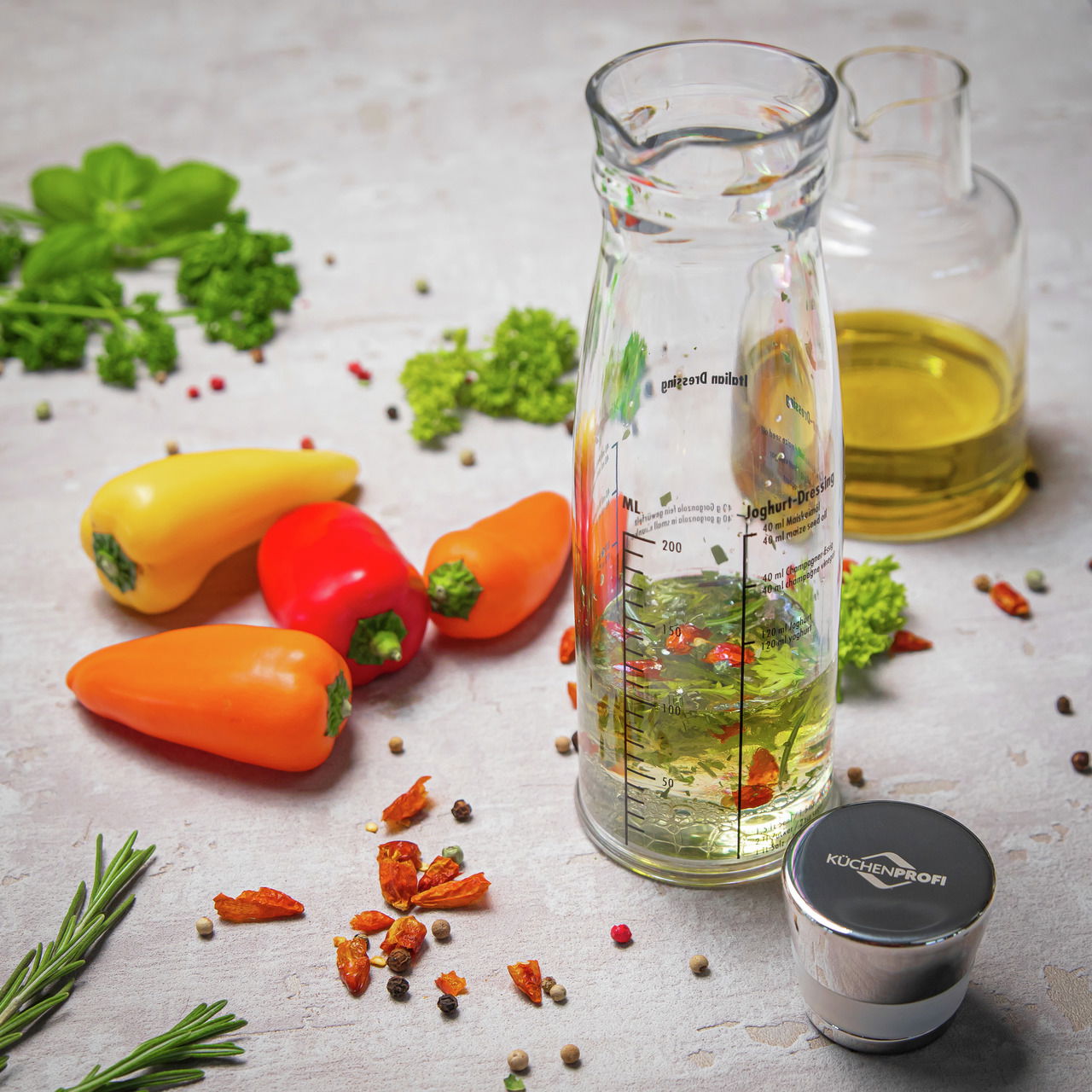 KÜCHENPROFI Dressing-Shaker Dressing-Shaker aus Glas mit Messskala, umgeben von frischen Paprikaschoten und Kräutern, aus der Vogelperspektive fotografiert.