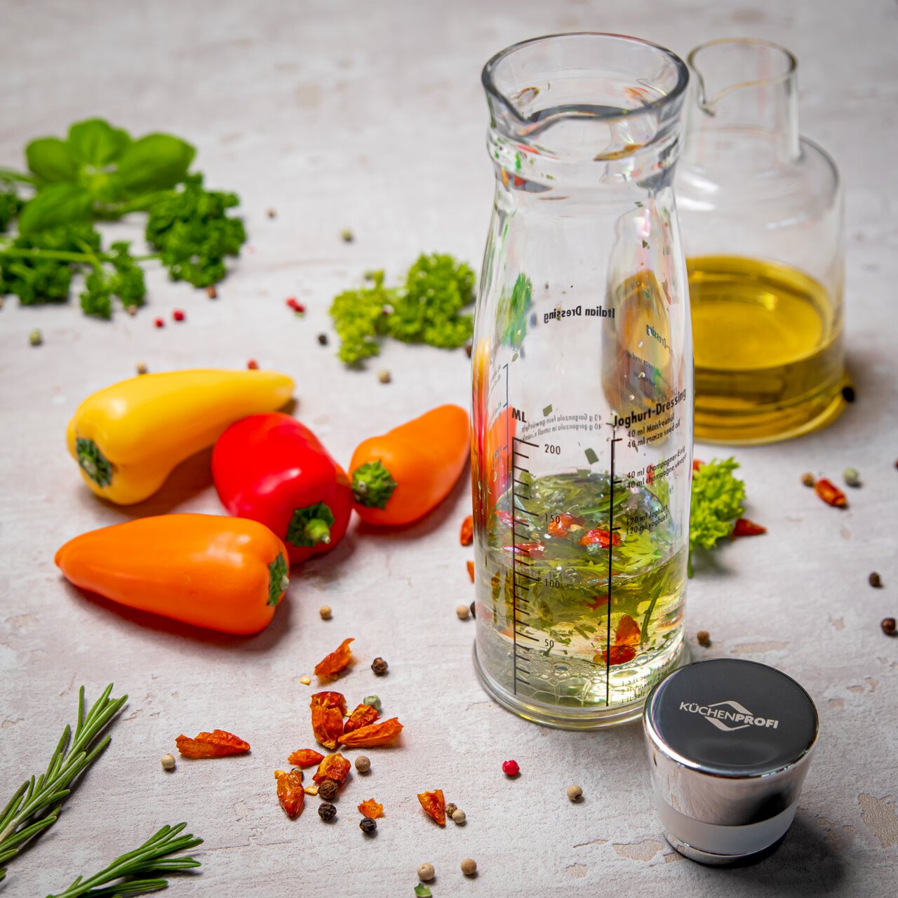 Dressing-Shaker aus Glas mit Messskala, umgeben von frischen Paprikaschoten und Kräutern, aus der Vogelperspektive fotografiert.