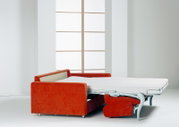 Orangefarbenes Schlafsofa mit ausgeklapptem Metallgestell und weißer Matratze, aus seitlicher Perspektive in einem hellen Wohnraum gezeigt