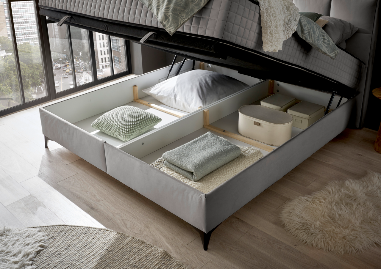 Boxbett mit geöffnetem Stauraum, gefüllt mit Kissen und Decken, aus der Perspektive eines Fensters mit Stadtblick.