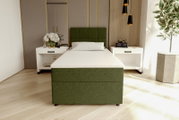 Modernes Einzelbett mit grün gepolstertem Kopf- und Fußteil sowie weißer Matratze, frontal in leichter Untersicht im Schlafzimmer zwischen zwei weißen Nachttischen fotografiert.