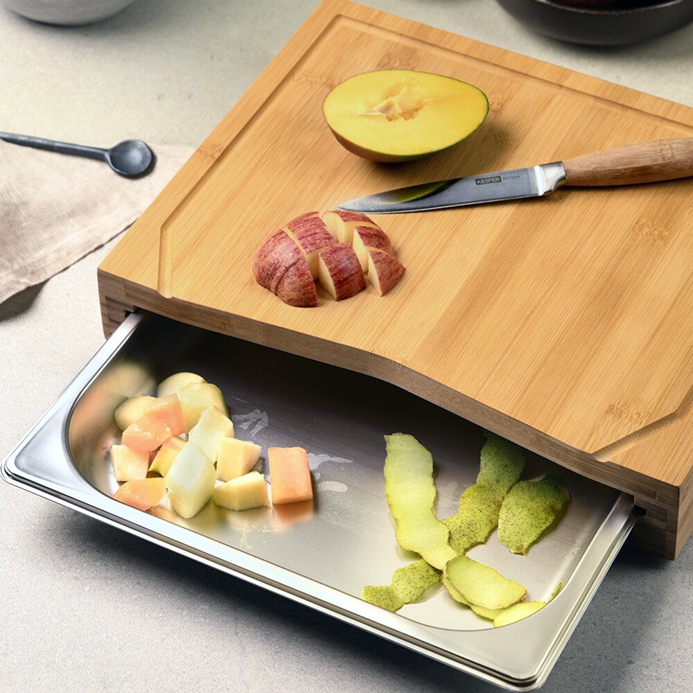 Schneidebrett aus Holz mit Auffangschale, darauf geschnittenes Obst und ein Messer, Perspektive von oben.