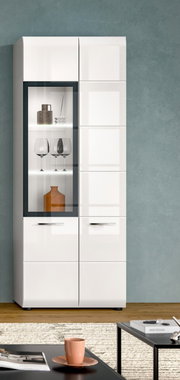 Moderne weiße Hochglanz-Vitrine/Schrank mit linksseitiger Glastür und beleuchteten Glasböden, darin Gläser und Deko, vor grauer Wand; frontale Ansicht.