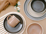 Vogelperspektive auf ein 16-teiliges Kombiservice-Set mit Tassen, Tellern und Schalen in Erdtönen, dekoriert mit weißen Blumen und einem braunen Tuch.