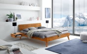 Modernes Bettgestell aus Holz in einem hellen, stilvollen Schlafzimmer mit Blick auf eine verschneite Berglandschaft durch große Fenster, seitliche Perspektive.