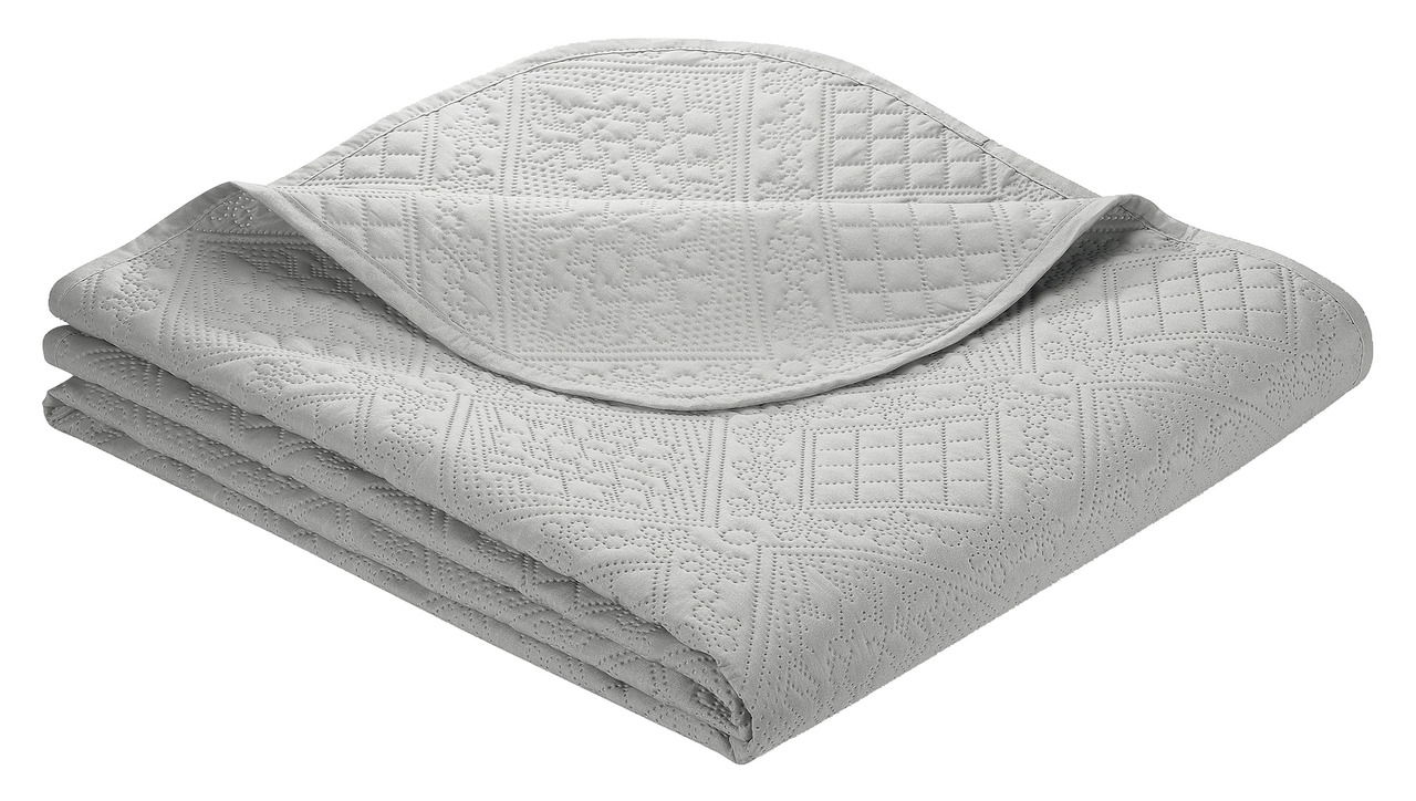 Graue Tagesdecke Nancy 220x250cm mit gestepptem Muster, gefaltet und aus einer schrägen Perspektive fotografiert.