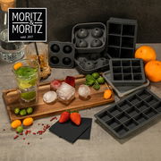 Verschiedene Eiswürfelformen und fertige Eiswürfel auf einem Tisch, mit Früchten und Getränken dekoriert. Perspektive von oben.