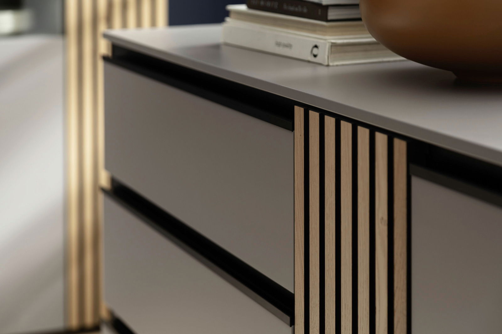 Nahaufnahme eines modernen Sideboards mit glatten, grauen Schubladen und vertikalen Holzlamellen an der Seite, von schräg vorne fotografiert.