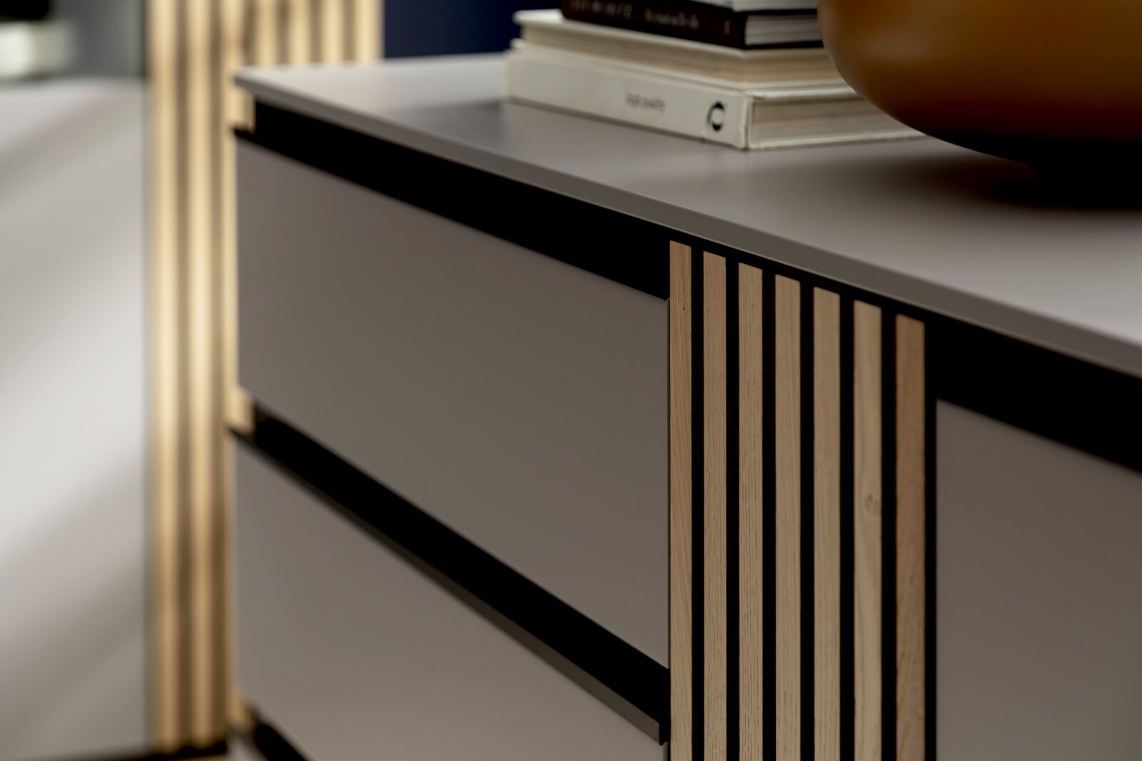 Close-up van een modern dressoir met gladde, grijze lades en verticale houten lamellen aan de zijkant, gefotografeerd vanuit een schuine hoek aan de voorkant.