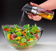 Essigsprüher/Ölspender in der Hand, der Öl auf einen frischen Salat in einer Glasschüssel sprüht, seitliche Perspektive.