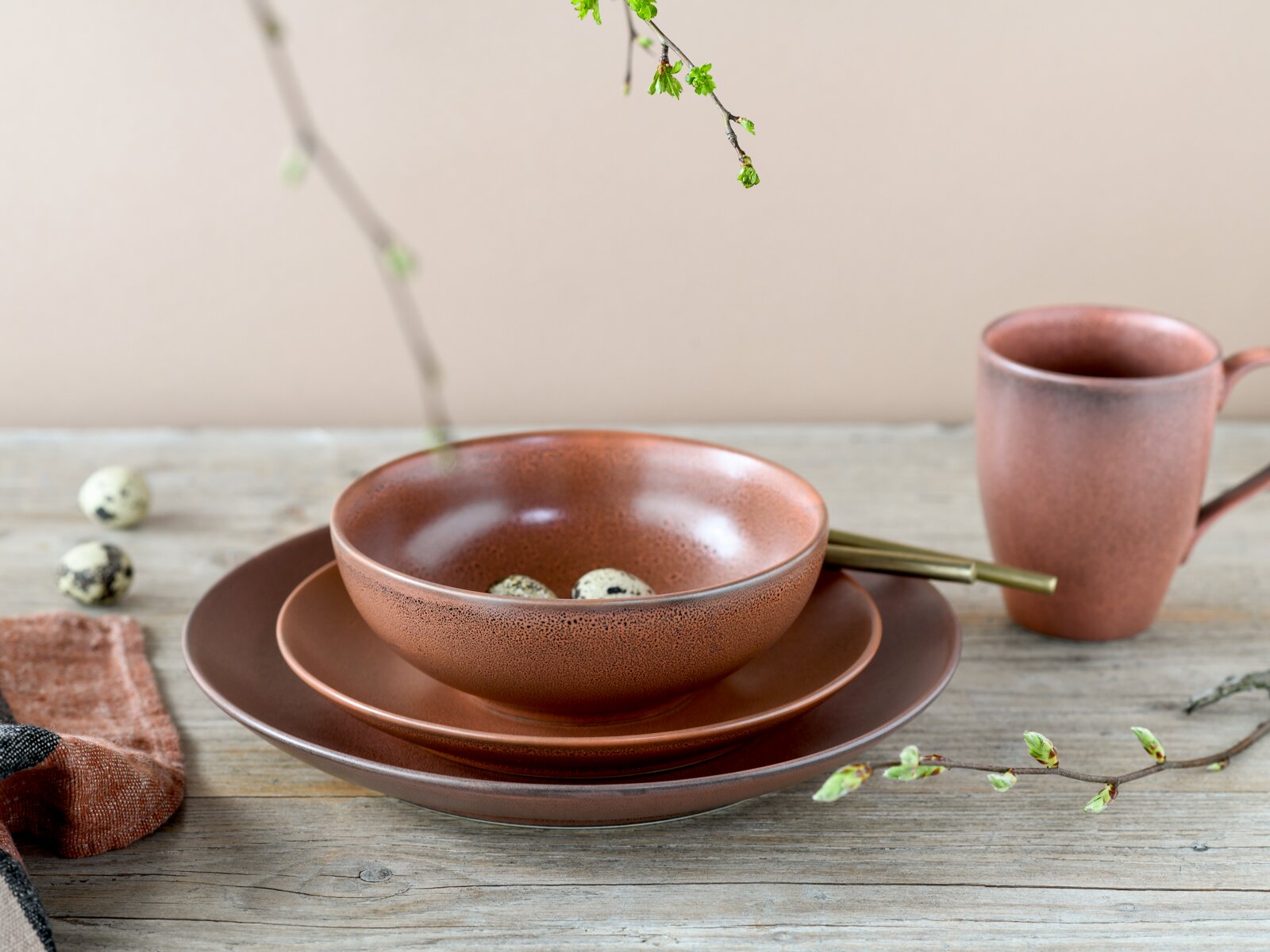 Rustikales braunes Keramikgeschirr-Set mit Schale auf zwei Tellern und passender Tasse auf Holztisch, perspektivisch in seitlicher Frontansicht leicht von oben fotografiert