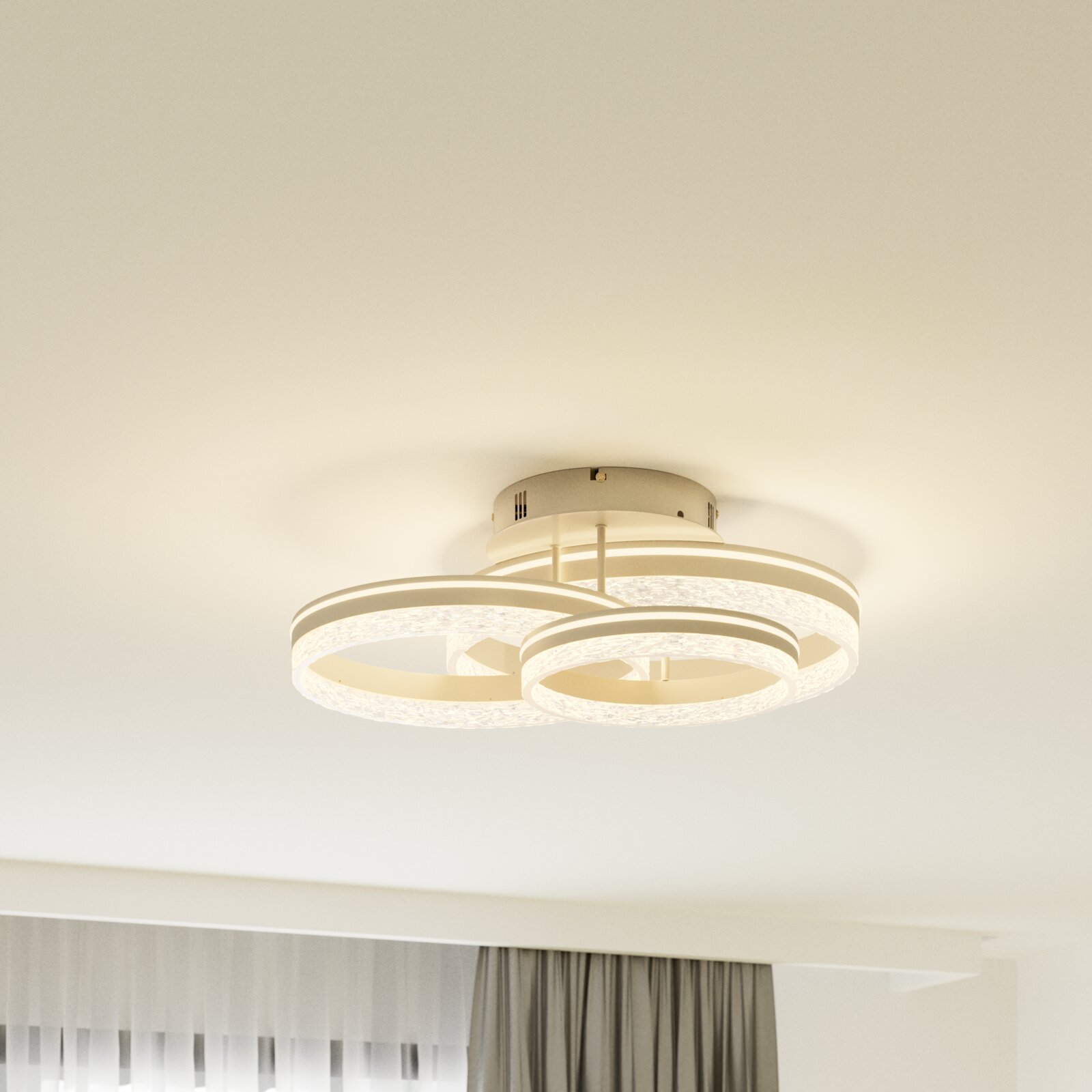 Moderne LED-Deckenleuchte in Weiß mit drei ringförmigen Lichtkreisen und kristallartiger Struktur, warmweiß leuchtend, Perspektive: leicht von unten zur Decke fotografiert