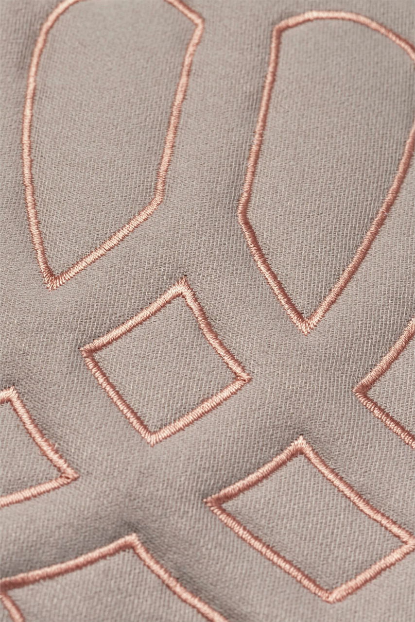 Nahaufnahme einer Zierkissenhülle mit geometrischem Stickmuster in Rosa auf beigem Stoff.