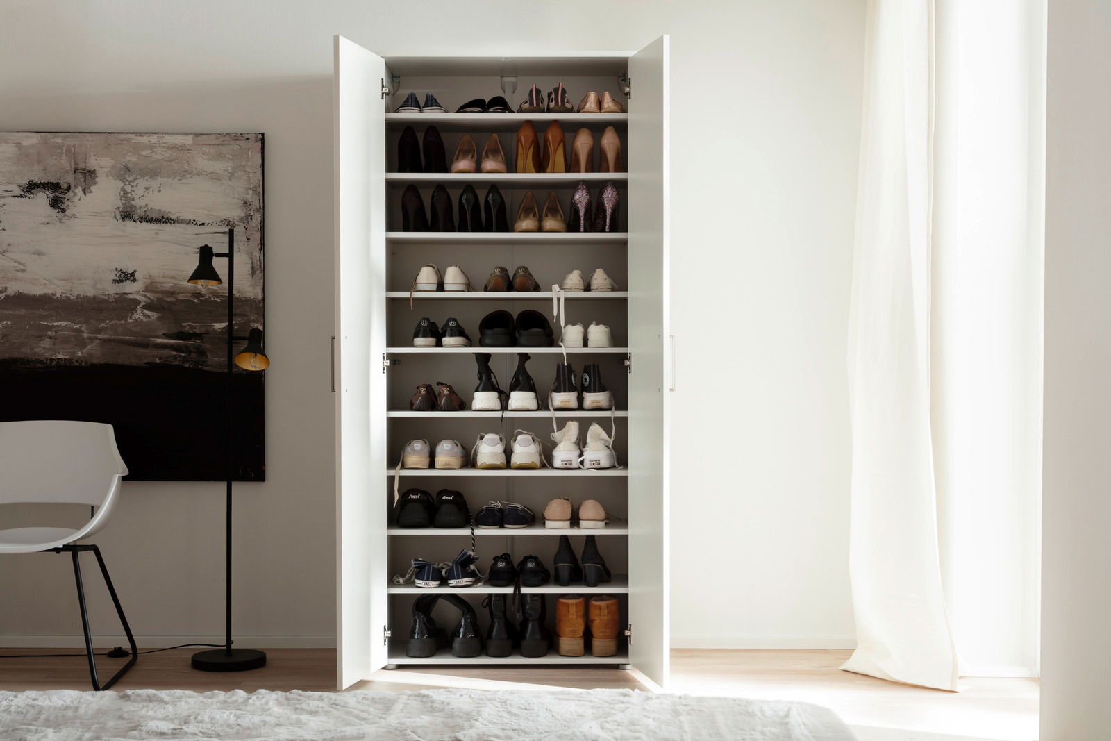 Offener, hoher Schuhschrank mit mehreren Regalböden, gefüllt mit verschiedenen Schuhen, in einem modernen, hellen Raum. Frontalansicht.