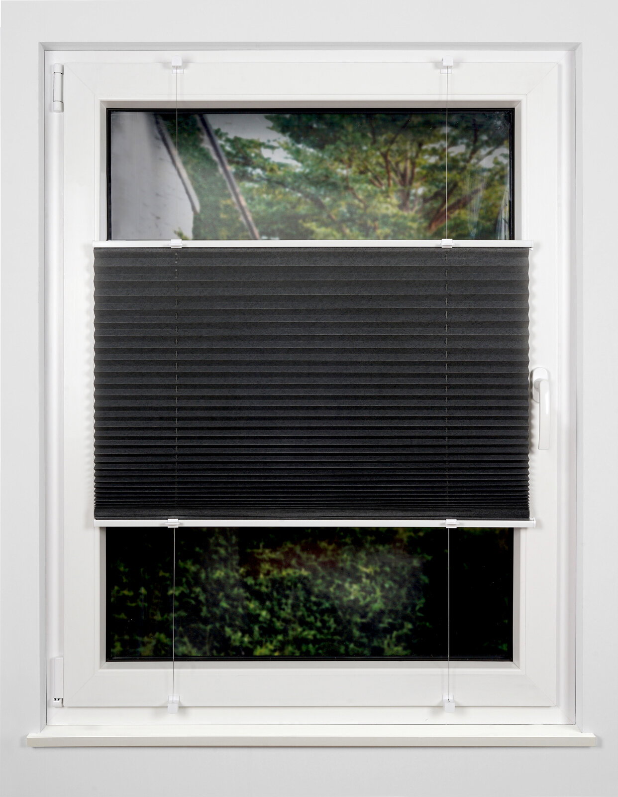 Schwarzes Plissee am Fenster, halb heruntergelassen, mit Blick auf einen Garten im Hintergrund.