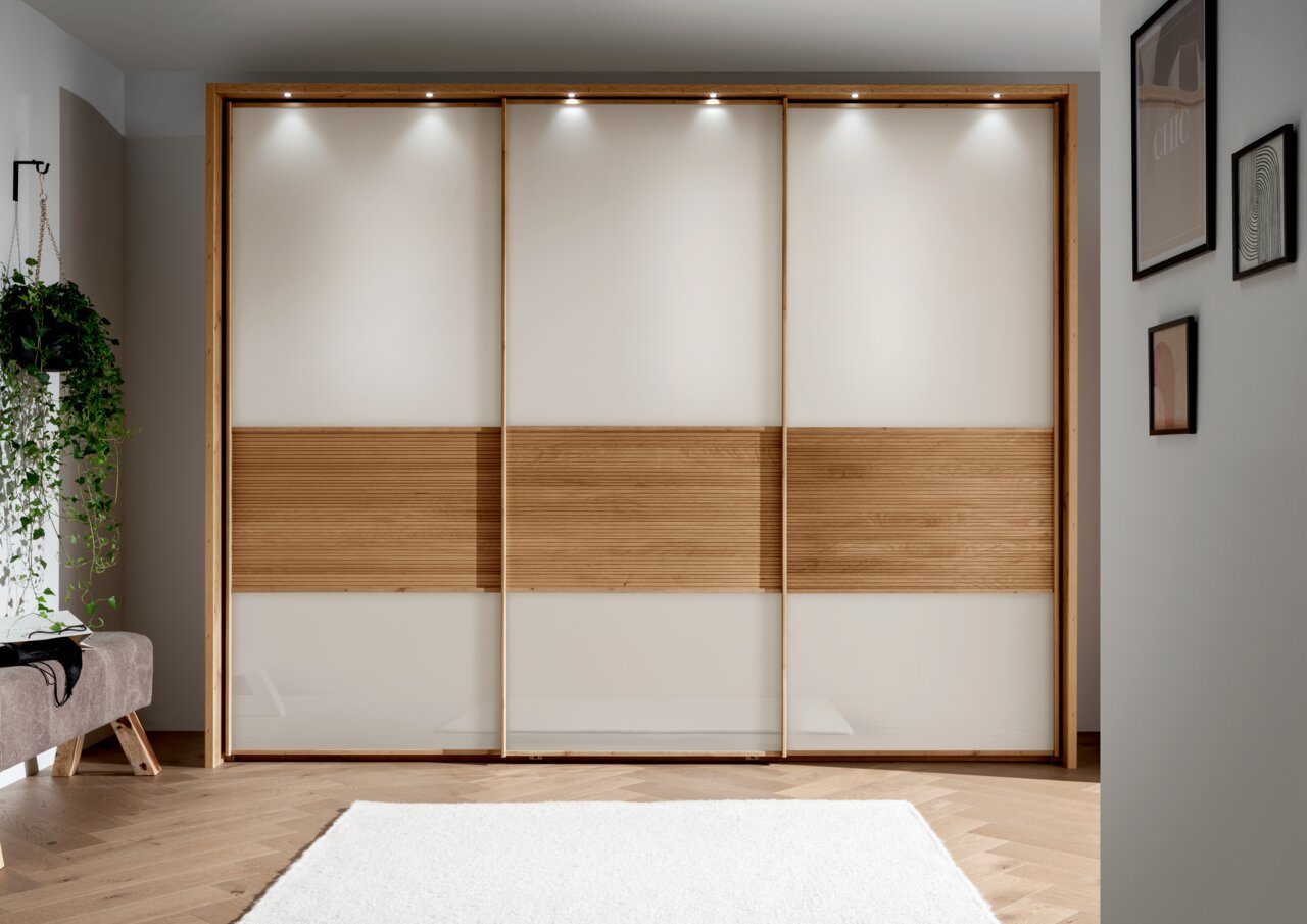 Moderne drievleugelige hangdeurkast met houten en glazen elementen, gefotografeerd van voren in een stijlvol ingerichte ruimte.
