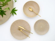 Beige Keramikteller-Set mit feiner radialer Rillenstruktur, arrangiert mit goldfarbenem Besteck auf weißem Hintergrund, Draufsicht von oben.