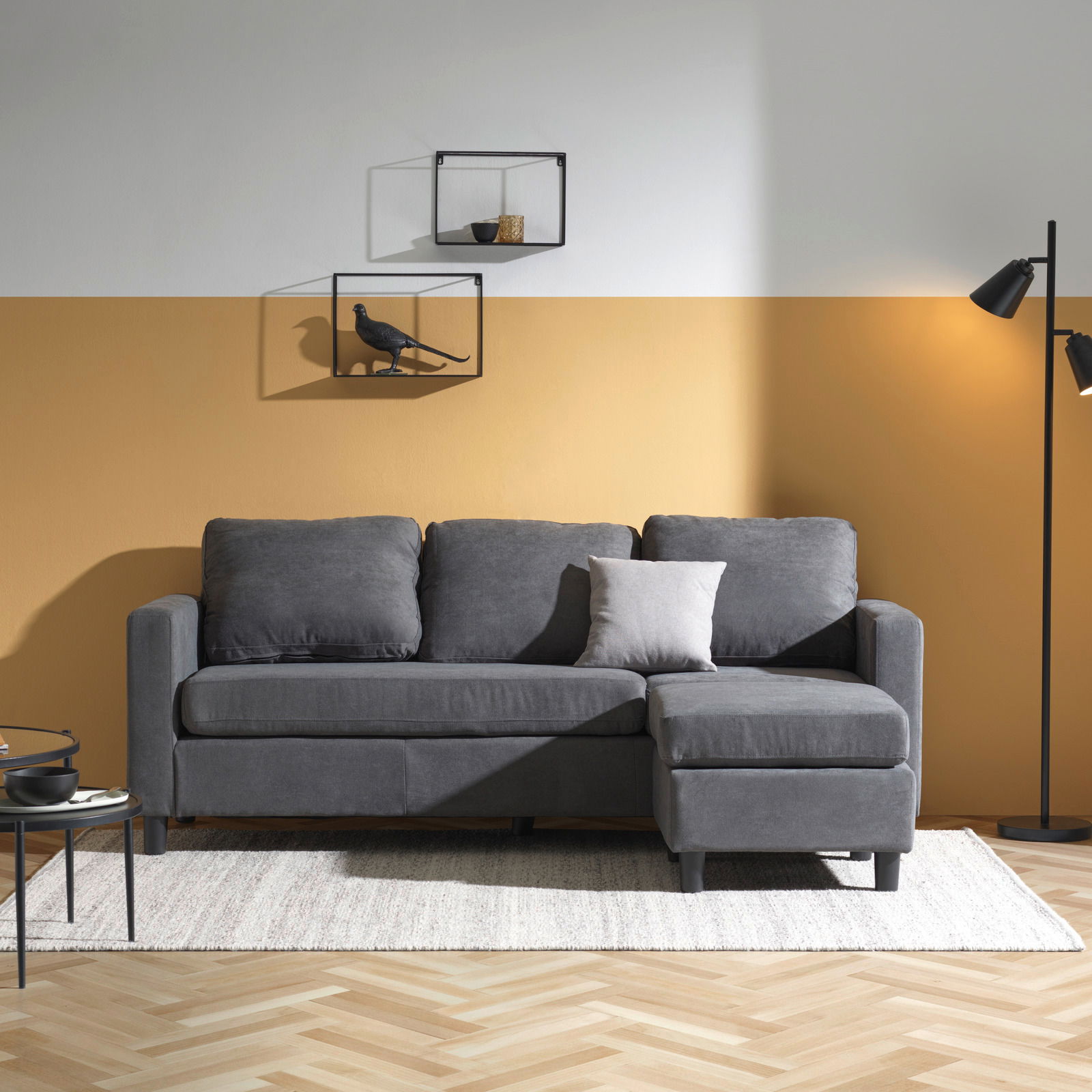 Ti´me Hoekbank TRIXI Graues Sofa mit Ottomane in einem modernen Wohnzimmer, frontal fotografiert.