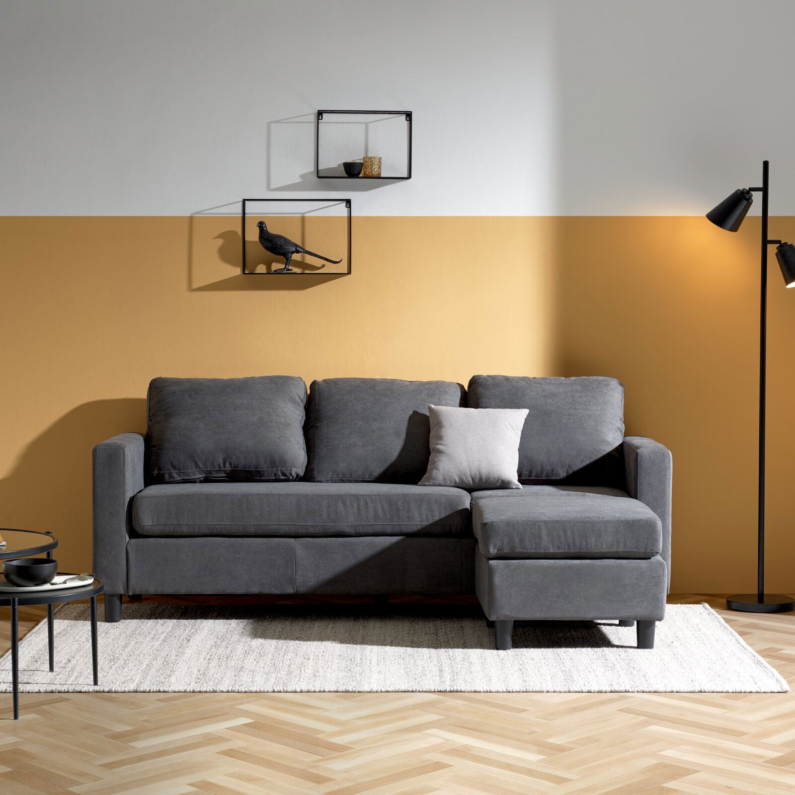 Graues Sofa mit Ottomane in einem modernen Wohnzimmer, frontal fotografiert.