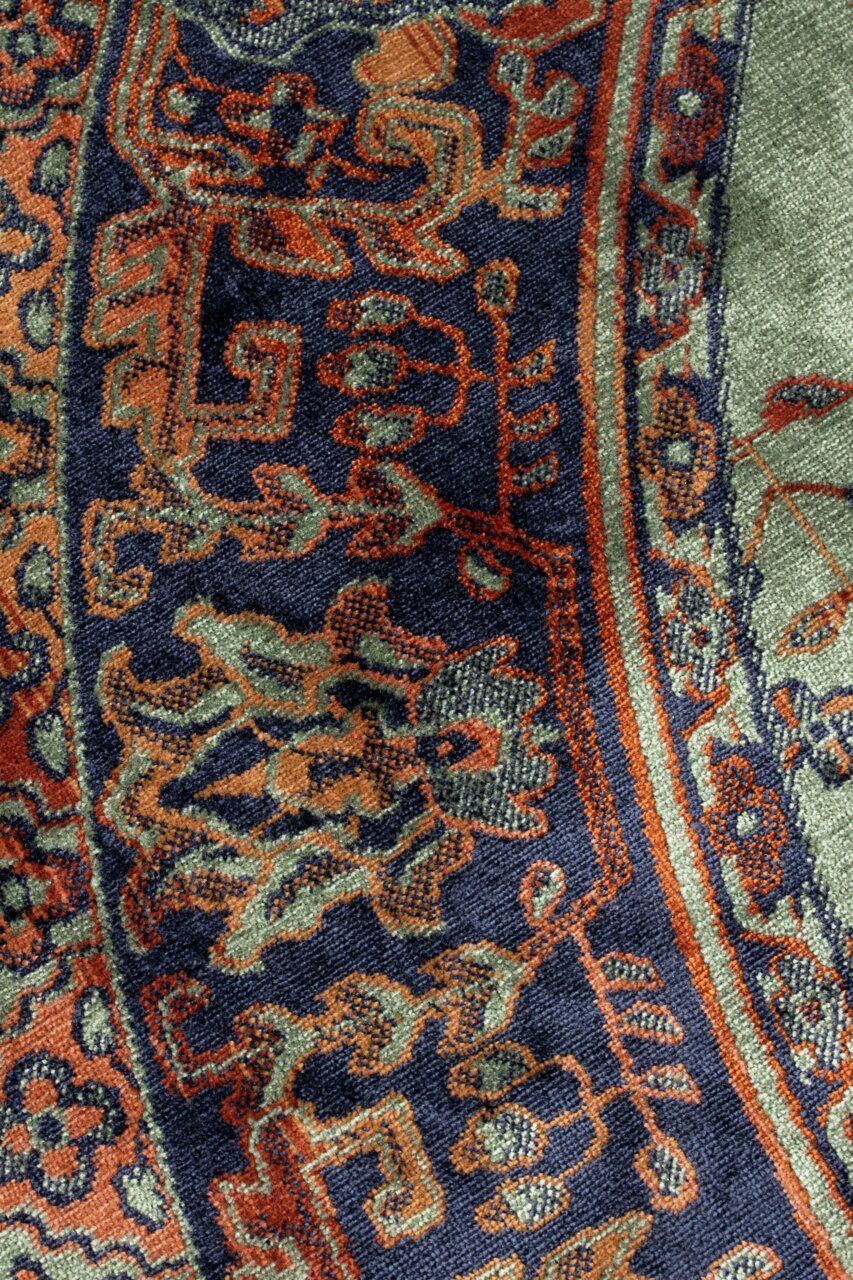 Nahaufnahme eines Teppichs mit orientalischem Muster in Blau, Orange und Grün, von oben betrachtet.