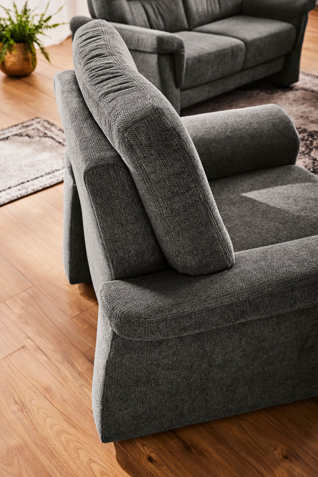 Grauer Sessel in Nahaufnahme, von schräg oben fotografiert, auf einem Holzboden mit einem Teppich im Hintergrund.