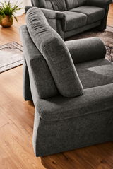 Grauer Sessel in Nahaufnahme, von schräg oben fotografiert, auf einem Holzboden mit einem Teppich im Hintergrund.