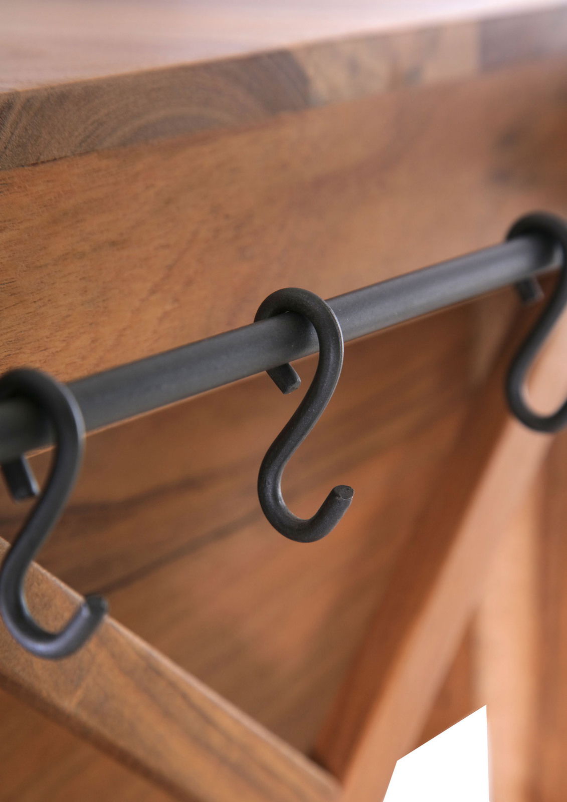 Nahaufnahme eines Servierwagens mit Holzoberfläche und schwarzen Haken an einer Metallstange, seitliche Perspektive.