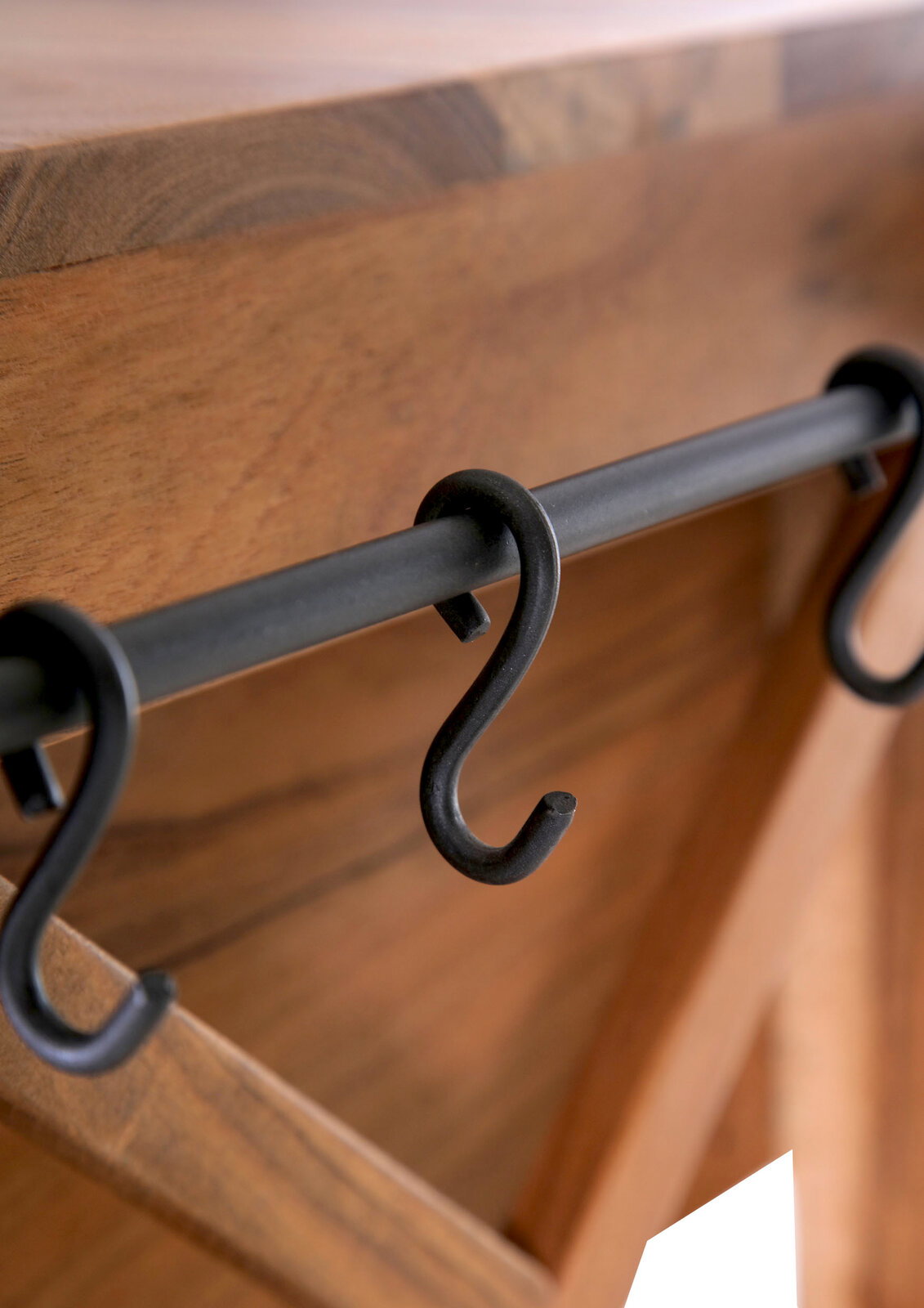 Nahaufnahme eines Servierwagens mit Holzoberfläche und schwarzen Haken an einer Metallstange, seitliche Perspektive.