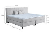 Graues Boxspringbett mit Kopfteil, drei Kissen und blauer Matratzenauflage, seitliche Perspektive