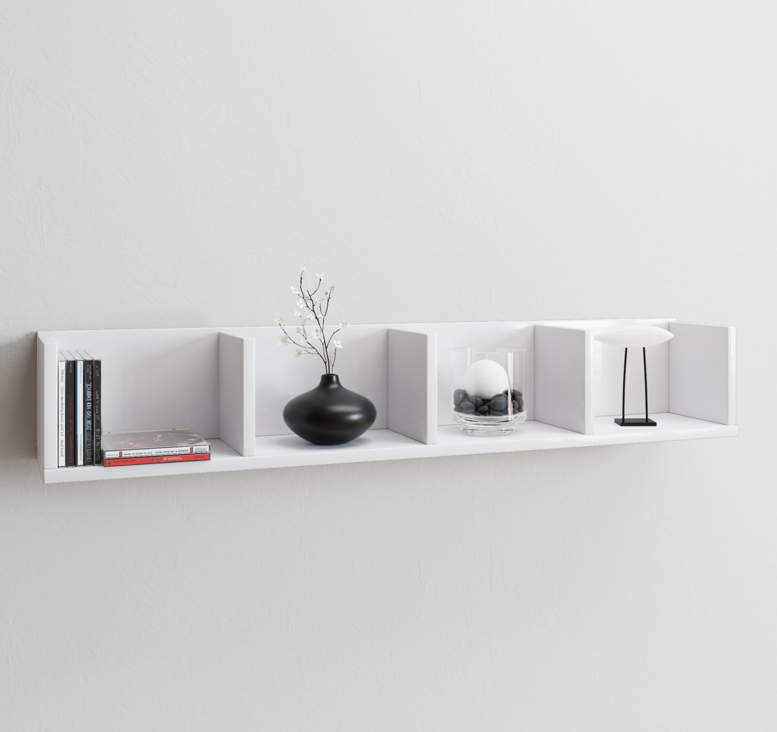 Weißes, wandmontiertes Regal mit Trennwänden, dekoriert mit Büchern, schwarzer Vase mit Zweig, Glasgefäß mit Steinen und Kugel sowie kleiner Lampe Frontansicht auf Augenhöhe.