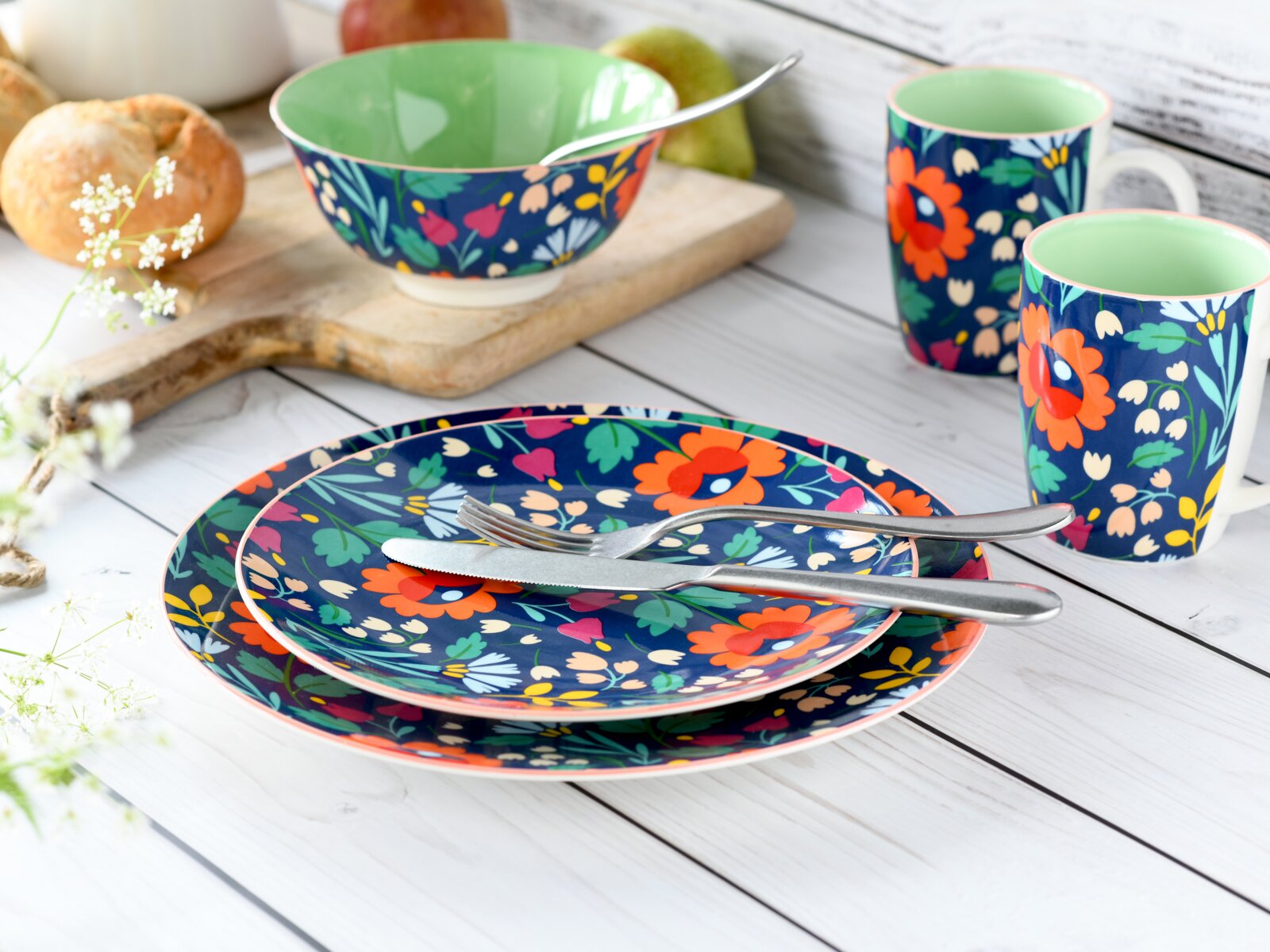 Creatable Tellerset 12-tlg FOLKLORE Buntes Geschirrset mit floralem Muster: zwei Teller, eine Schüssel und zwei Tassen in Blau mit roten Blumen und mintgrünem Innenraum, auf weißem Holztisch arrangiert, Perspektive leicht von oben schräg.