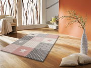 Teppich mit Stern- und Herzmustern in Rosa und Grau auf Holzboden, perspektivisch von schräg oben fotografiert.