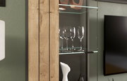 Detailansicht einer Vitrine mit Holztür und Glaseinlegeböden, auf denen Weingläser und Dekorationsobjekte stehen.