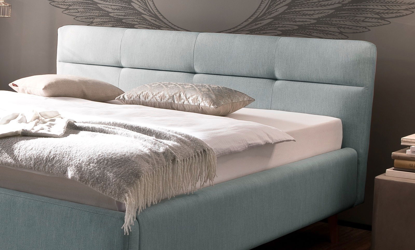 Polsterbett in hellblauem Stoff mit gestepptem Kopfteil, seitliche Perspektive