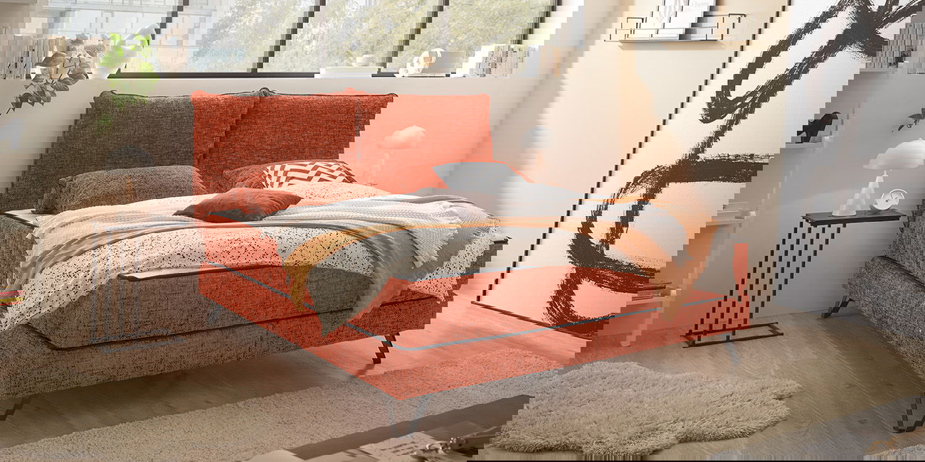 Ein helles Schlafzimmer mit einem Polsterbett in der Farbe Terrakotta.