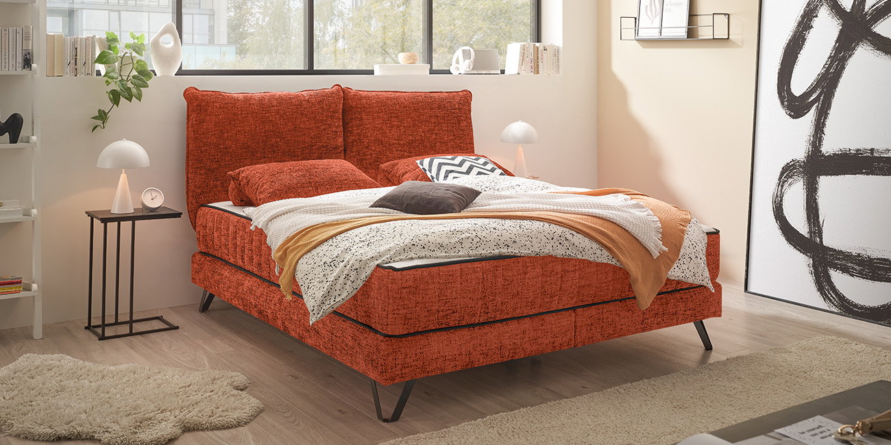 Ein helles Schlafzimmer mit einem Polsterbett in der Farbe Terrakotta.