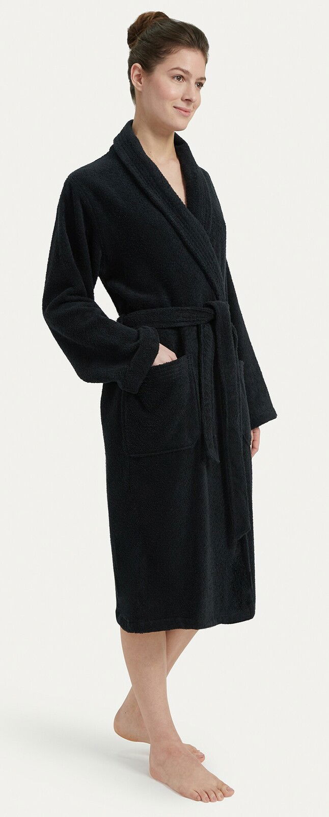 Frau in einem schwarzen Bademantel mit Schalkragen, stehend in einer seitlichen Perspektive.