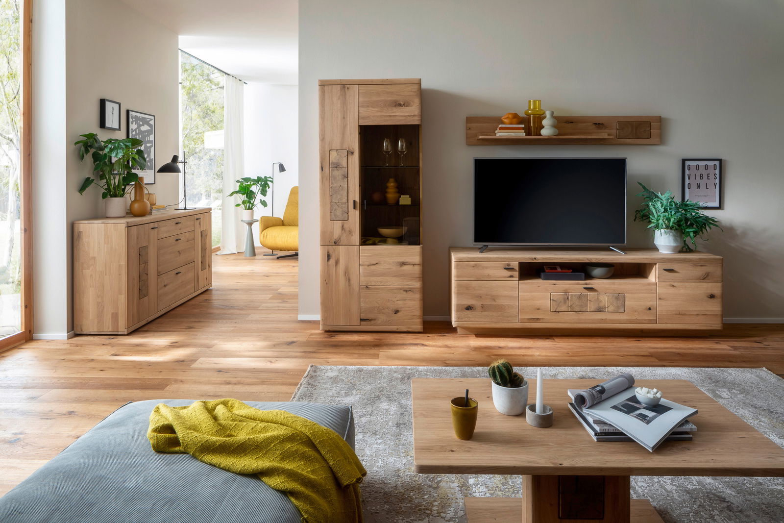 Wohnzimmer mit moderner Holzmöbelkombination, bestehend aus Sideboard, Vitrine und Wandregal, aus hellem Holz. Perspektive von vorne.