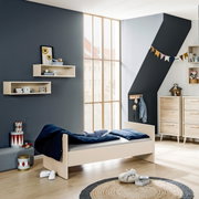 Kinderkamer met een eenpersoonsbed van lichtgekleurd hout, gezien vanaf de zijkant, omringd door moderne meubels en decoraties.