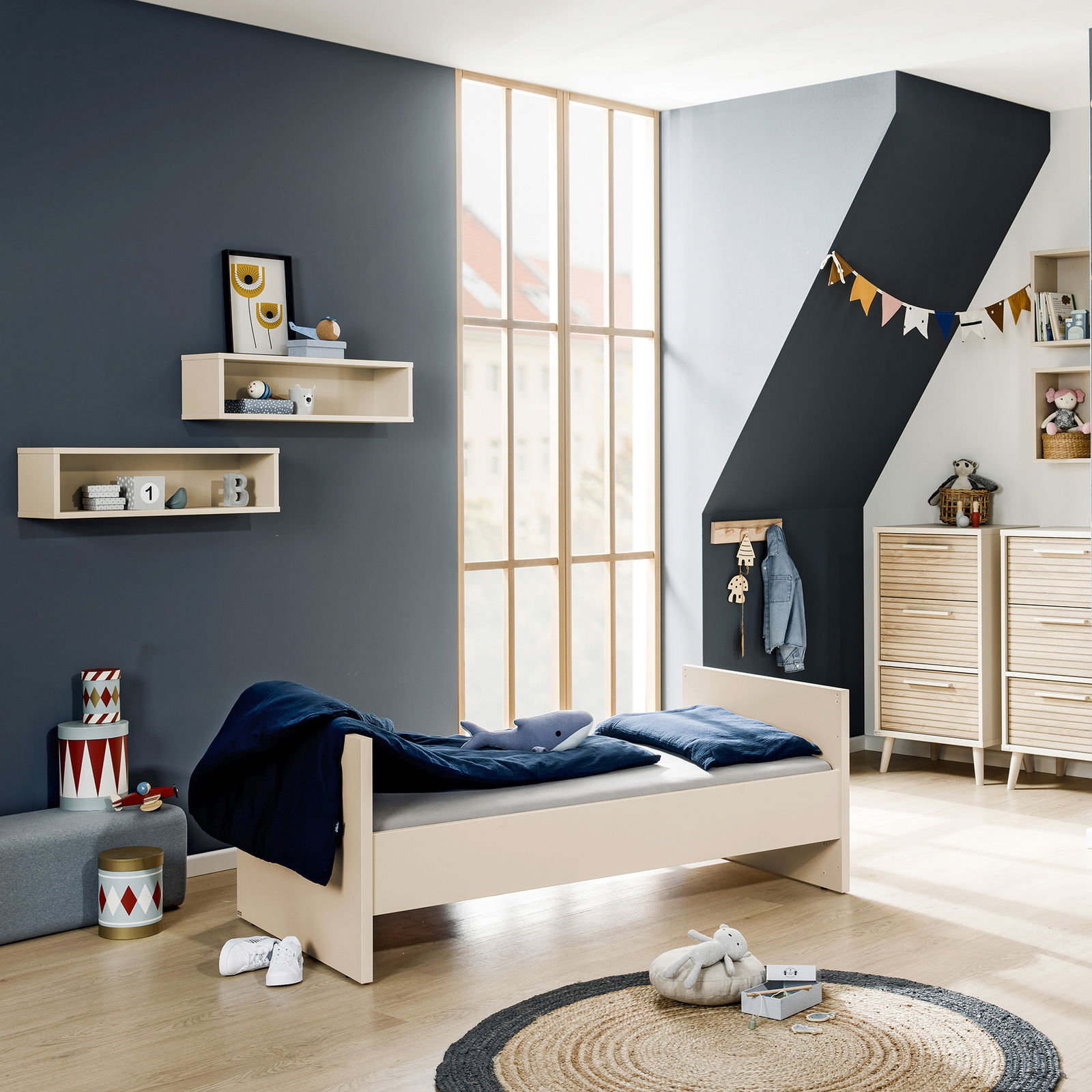 Kinderzimmer mit einem Einzelbett in hellem Holz, von der Seite betrachtet, umgeben von modernen Möbeln und Dekorationen.