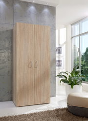 Moderner Kleiderschrank aus Holz in heller Eichenoptik, frontal fotografiert, in einem hellen Raum mit großen Fenstern und Pflanzen.