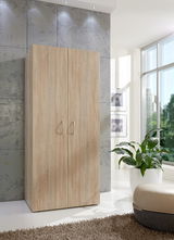 Moderner Kleiderschrank aus Holz in heller Eichenoptik, frontal fotografiert, in einem hellen Raum mit großen Fenstern und Pflanzen.