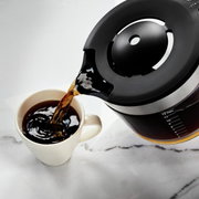 Kaffeemaschine Empire rot: Nahaufnahme einer Kaffeekanne, die Kaffee in eine Tasse gießt, von oben betrachtet.