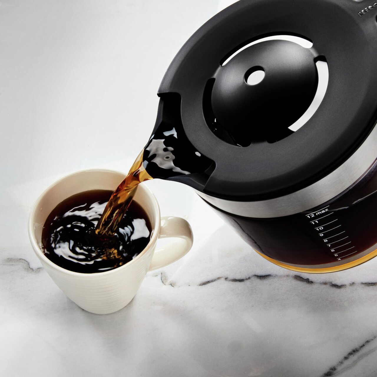 Kaffeemaschine Empire rot: Nahaufnahme einer Kaffeekanne, die Kaffee in eine Tasse gießt, von oben betrachtet.
